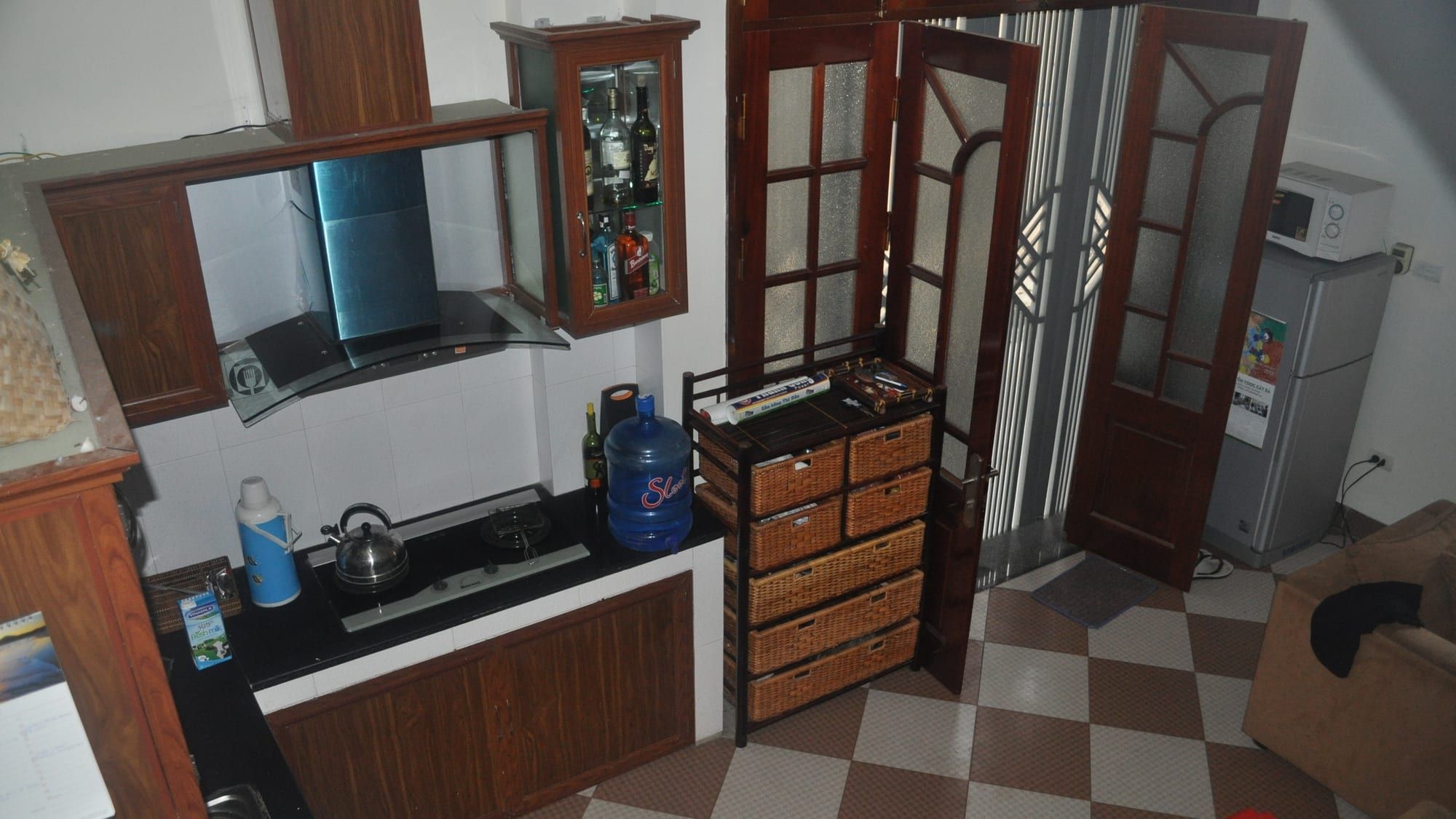 A compact kitchen with dark-wood cabinets, a black counter with a gas hob and kettle under a glass range hood, and a checkered tile floor.